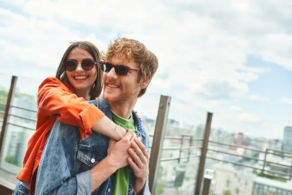 Un hombre abraza a una mujer en la azotea de un rascacielos, contra un escenario escénico de la ciudad, que simboliza el amor, la confianza y la aventura - foto de stock