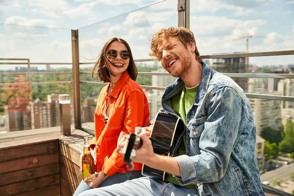 Мужчина и женщина сидят на крыше здания, наслаждаясь видом на город под ними в солнечный день — стоковое фото