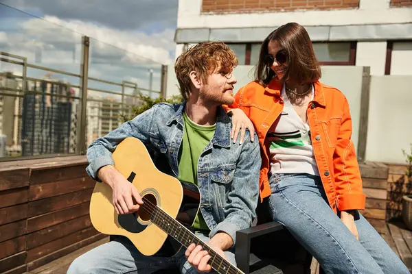 A man sitting next to a woman, serenading her with a guitar while enjoying the sunset together — Stock Photo