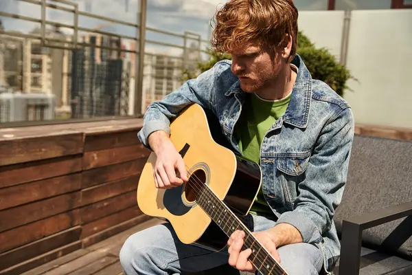 Un hombre talentoso se sienta en un banco, tocando apasionadamente una guitarra, perdido en la música bajo el cielo abierto - foto de stock