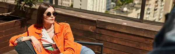 A woman in an orange jacket sits peacefully on a wooden bench, enjoying a moment of relaxation in a serene outdoor setting — Stock Photo