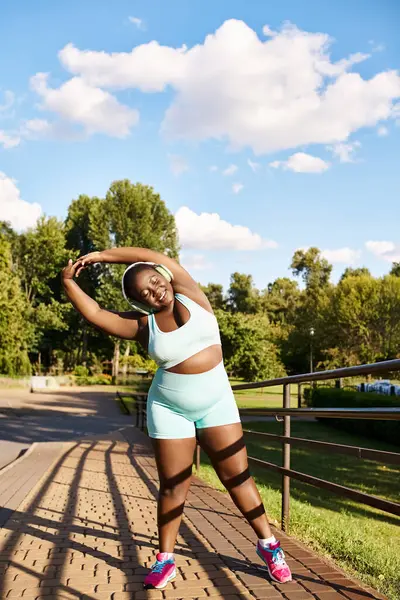 An African American woman in blue shorts and a white tank top stretches her arms outdoors — Stock Photo