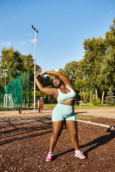 An African American woman in sports bra and shorts stretches outdoors, showcasing body positivity and strength. — Stock Photo