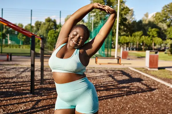 Eine Afroamerikanerin mit kurvigem Körper, in blauem Sport-BH, die Arme im Freien ausstreckt. — Stockfoto