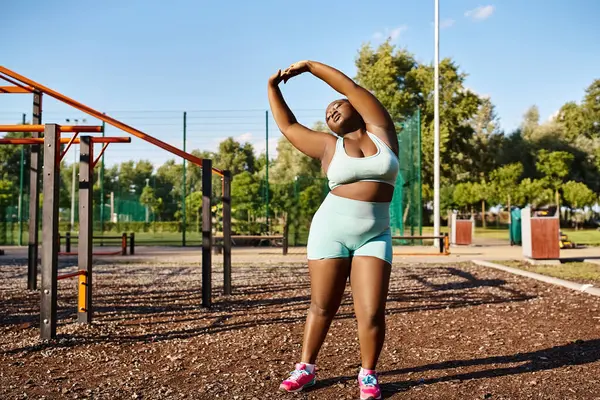 An African American woman in blue sports bra and shorts stands confidently in front of a playground. — Stock Photo