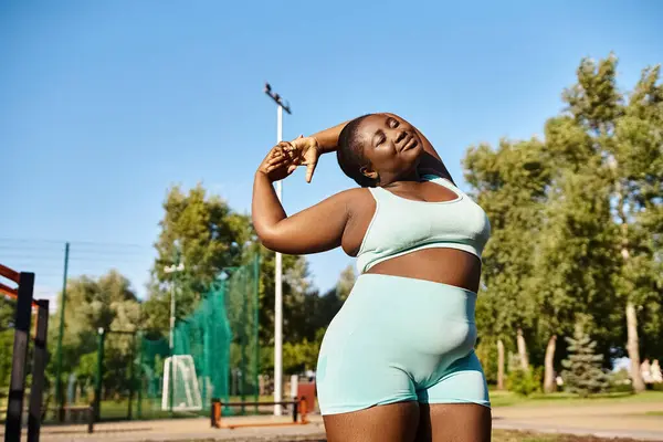 A curvy African American woman in sportswear confidently stretching her arms outdoors, exuding strength and determination. — Stock Photo