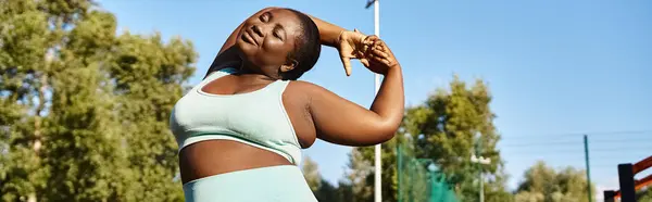 Une Afro-Américaine en tenue de sport étirant les bras à l'extérieur, embrassant sa positivité corporelle. — Photo de stock