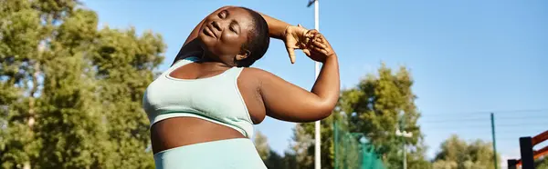 Una mujer afroamericana en ropa deportiva estira con confianza sus brazos al aire libre, abrazando su positividad corporal. — Stock Photo
