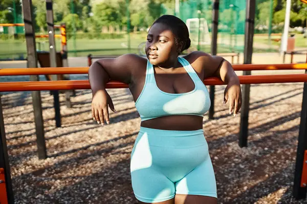 Una mujer afroamericana en ropa deportiva felizmente se para frente a un patio de recreo, encarnando la positividad corporal y el empoderamiento. - foto de stock