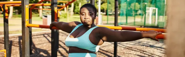 An African American woman in sportswear standing in front of a playground, showcasing body positivity and strength. — Stock Photo