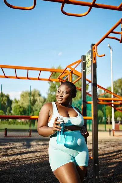 Uma mulher afro-americana em um sportswear azul e branco corre na frente de um playground, mostrando positividade do corpo e confiança. — Fotografia de Stock