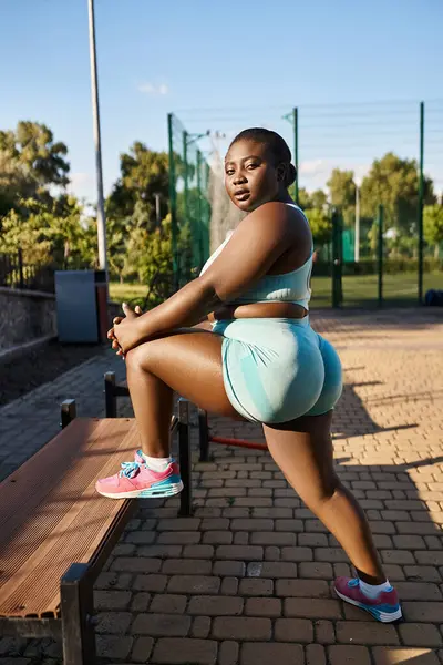 An African American woman in sportswear working out gracefully on a wooden bench, surrounded by nature, embodying body positivity. — Stock Photo