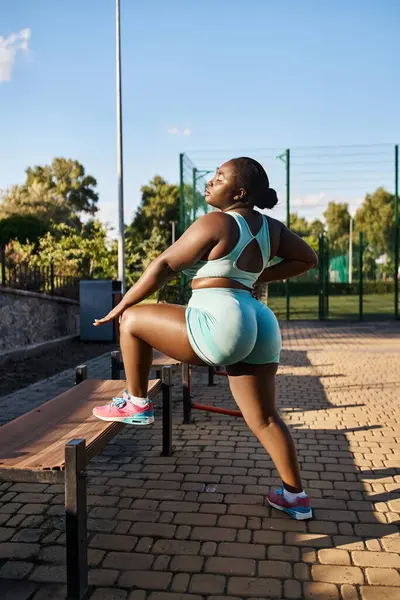 Una donna afroamericana in abbigliamento sportivo si siede tranquillamente su una panchina, abbracciando un momento di calma all'aria aperta, allenandosi — Foto stock