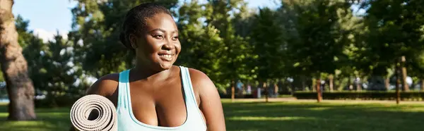Eine Afroamerikanerin, körperbetont und kurvig, hält in einem ruhigen Park eine Yogamatte in der Hand. — Stockfoto