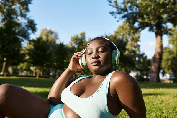 Una donna afroamericana in abbigliamento sportivo giace sull'erba, profondamente immersa nella sua musica. — Foto stock