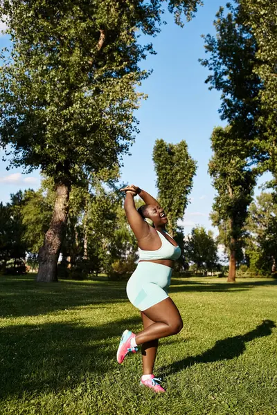 Mujer curvilínea en top blanco y pantalones cortos azules practicando yoga al aire libre, encarnando positividad corporal y autocuidado. - foto de stock