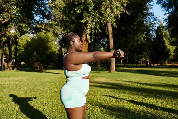 An African American woman in a blue skillfully holds a dumbbells outdoors. — Stock Photo