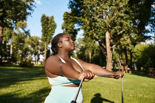 Афроамериканка в спортивной одежде уверенно держит скакалку, готовую к качелям в живописном парке. — стоковое фото