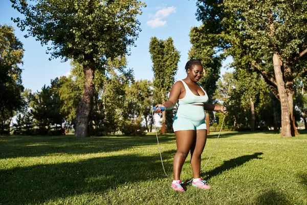Una mujer afroamericana en ropa deportiva explora su potencial corporal, empuñando con gracia una cuerda para saltar al aire libre. - foto de stock