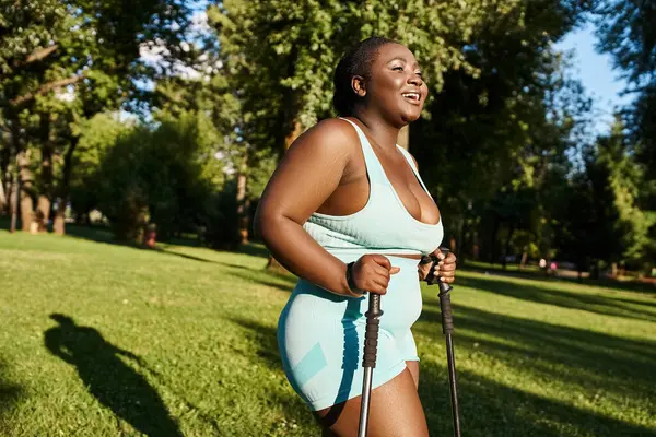 An African American woman in a blue swimsuit enjoys a sunny day outdoors while holding walking sticks — Stock Photo