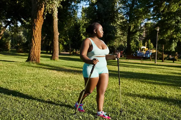 Una mujer afroamericana en ropa deportiva está de pie en la hierba, sosteniendo con confianza un bastón. - foto de stock