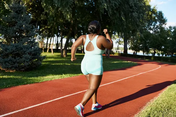 Афроамериканка в спортивной одежде бежит по красной дорожке, демонстрируя позитивность тела и атлетизм.. — стоковое фото