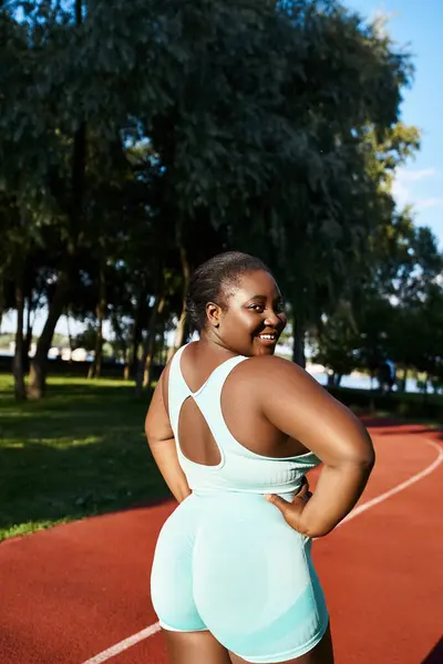 Una mujer afroamericana está de pie con confianza en una cancha, mostrando su atletismo y fuerza. - foto de stock