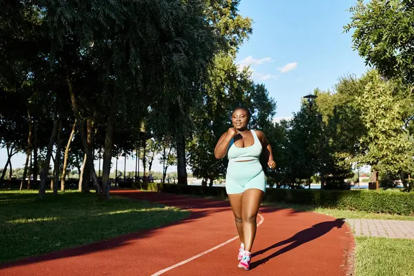 Una mujer afroamericana con curvas en ropa deportiva corriendo sobre una vibrante pista roja. - foto de stock