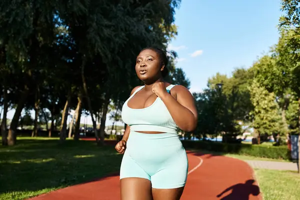 Una mujer afroamericana con curvas se ejercita con confianza al aire libre con un sujetador deportivo azul y pantalones cortos. - foto de stock