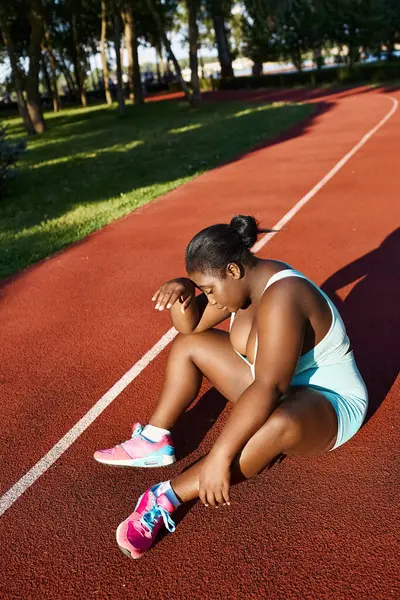 Una joven afroamericana en ropa deportiva se sienta con gracia en la cancha de tenis, encarnando fuerza y confianza. - foto de stock