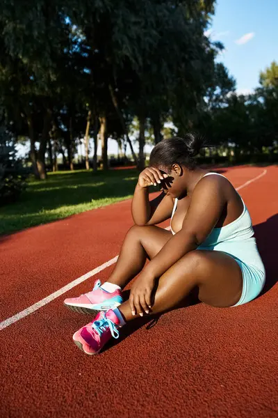 An African American woman in sportswear sits on a tennis court, deep in thought, embracing her curves and embodying body positivity. — Stock Photo