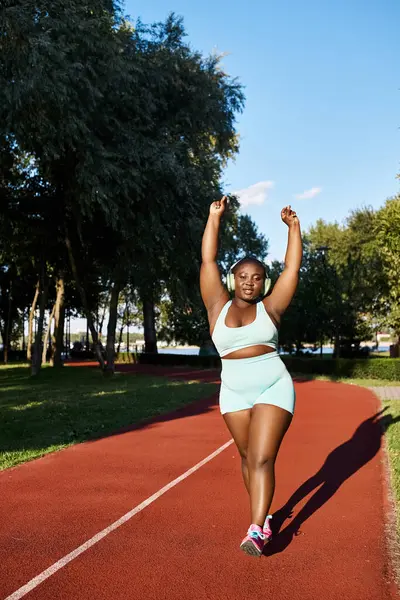 Une Afro-Américaine en tenue de sport court sur une piste, montrant son athlétisme et sa positivité corporelle. — Photo de stock