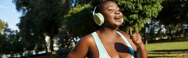 An African American woman in sportswear, with a body positive attitude, standing in a park while wearing headphones. — Stock Photo