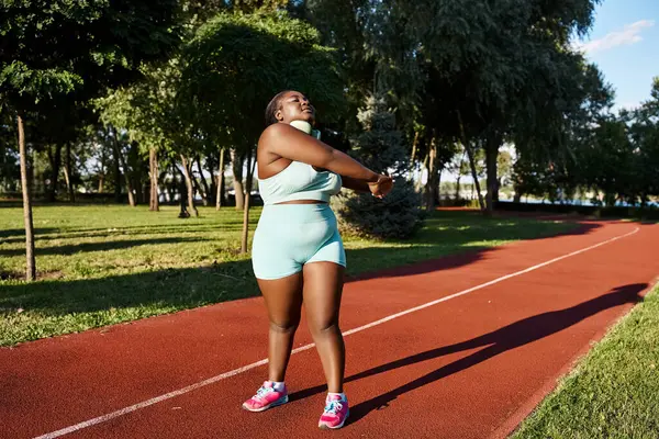Africano mulher americana com um corpo curvilíneo fica em uma pista, aquecendo — Fotografia de Stock