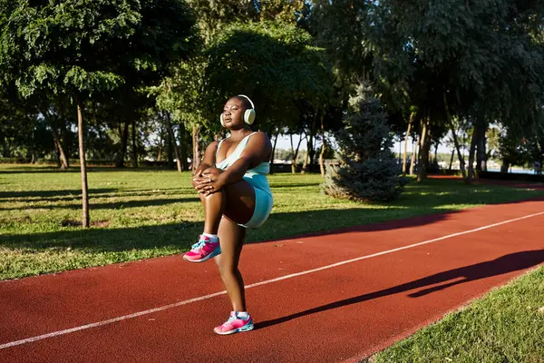 Uma mulher afro-americana em sportswear está com os braços cruzados em uma pista, exalando confiança e força. — Fotografia de Stock