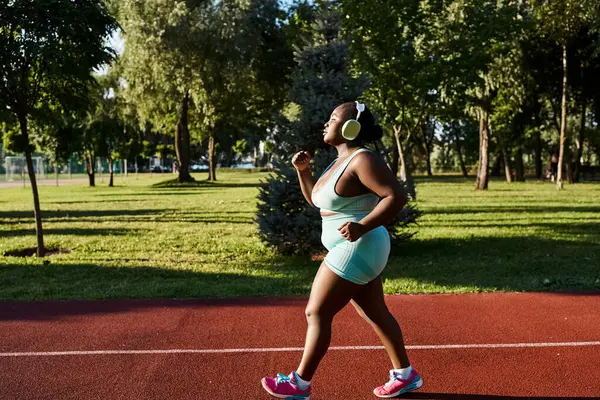 Une Afro-Américaine en tenue de sport, célébrant ses courbes, court gracieusement sur un court de tennis dans un cadre extérieur. — Photo de stock