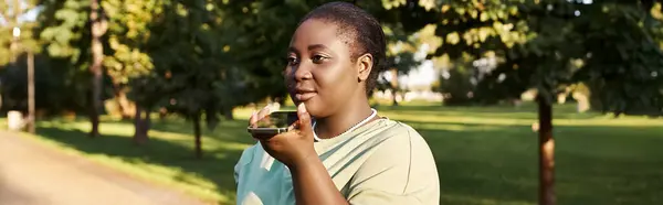 Eine junge Frau, Plus Size und Afroamerikanerin, hält im Sommer draußen im Freien ein Smartphone in der Hand und umarmt Körperpositivität. — Stockfoto