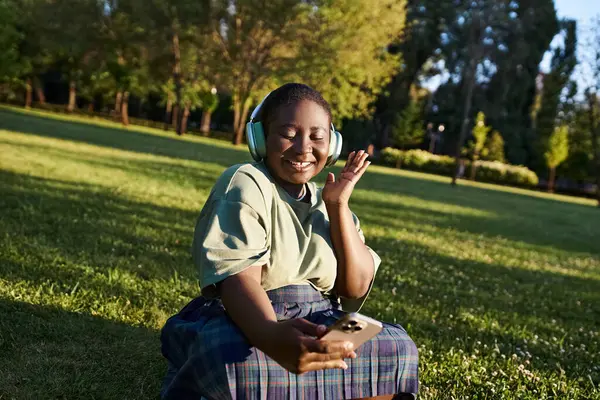 A plus-size African American woman enjoying music while seated on grass in casual attire, embracing body positivity. — Stock Photo