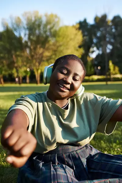 Frau entspannt sich im Gras, eingetaucht in Musik, die an einem sonnigen Tag über Kopfhörer gespielt wird. — Stockfoto