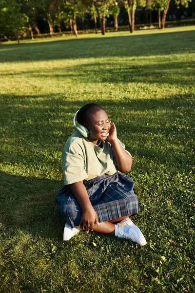 Frau entspannt sich im Gras, eingetaucht in Musik, die über Kopfhörer abgespielt wird — Stockfoto