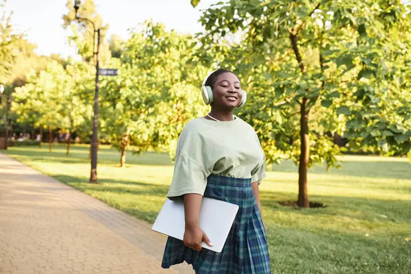 A plus size African American woman in casual attire walks confidently on a park sidewalk in summer. — Stock Photo