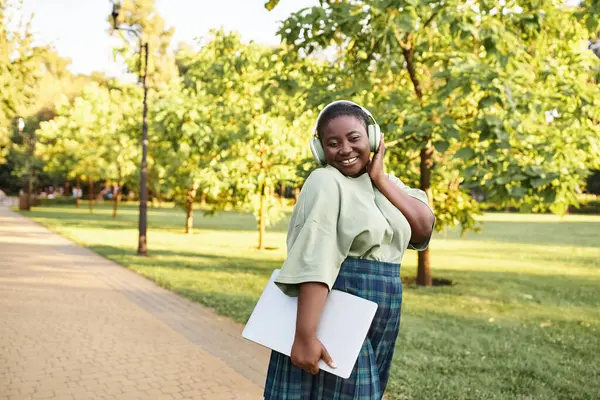 A plus-size African American woman in casual attire, wearing a green shirt and plaid skirt, outdoors in the summer. — Stock Photo