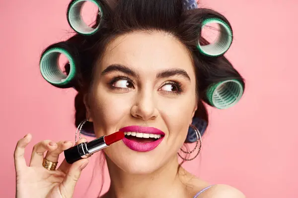 Woman with curlers in hair holds lipstick in front of face. — Stock Photo