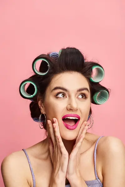 A woman with curlers in her hair poses against a vibrant backdrop. — Stock Photo