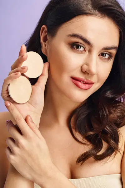 Una mujer impresionante con belleza natural aplicando maquillaje usando un compacto. - foto de stock