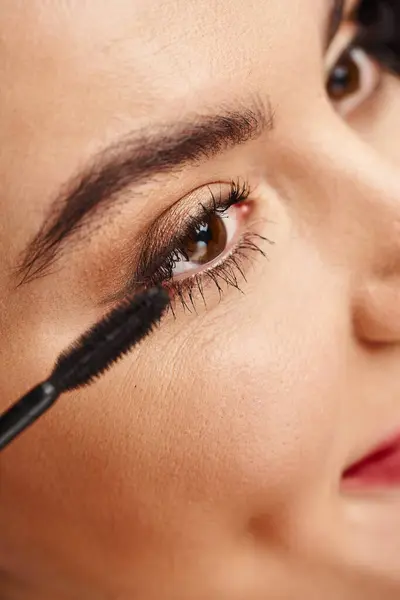 Close-up portrait of an attractive woman applying makeup with a mascara near her eye. — Stock Photo