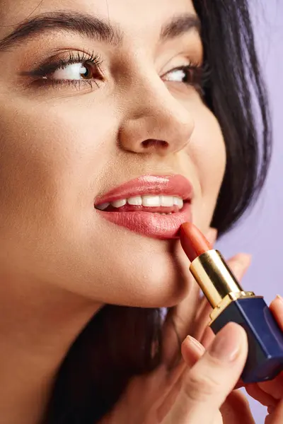 A stunning woman gracefully applies lipstick to her lips. — Stock Photo