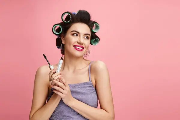 Mulher elegante com encrespadores no cabelo mantém rímel, aplicando maquiagem com precisão. — Fotografia de Stock