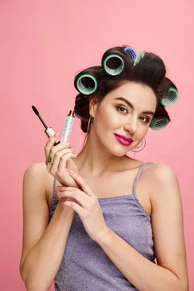 A woman with curlers in her hair applies mascara. — Stock Photo