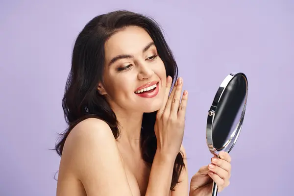 A woman holding a mirror, smiling while applying makeup. — Stock Photo